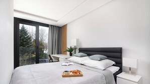A modern bedroom with a large bed, a bedside table with a lamp, and a tray with croissants and coffee. - EASY RENT Apartments - AMBER 10 (Lublin)
