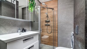 A modern bathroom with a glass-enclosed shower, a white sink with a mirror above, and a wooden panel wall. - EASY RENT Apartments - AMBER 10 (Lublin)