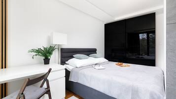 A modern bedroom with a bed, bedside table, chair, and a potted plant.