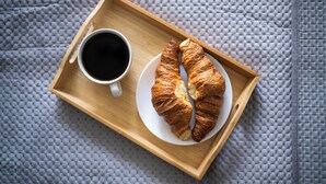 A wooden tray with a croissant and a cup of coffee on a textured grey surface. - EASY RENT Apartments - AMBER 10 (Lublin)