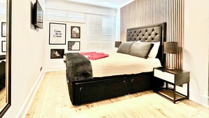 A modern bedroom with a bed, bedside table, and wall-mounted TV. - Clapham 3-bed Flat, Sleeps 6 With Free Parking (London)