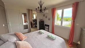 Un dormitorio con una cama grande, un aparador, una silla, un espejo y vistas al exterior.