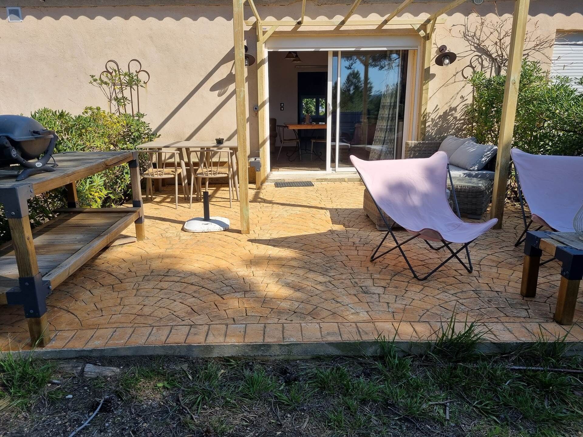 Un patio exterior con mesa y sillas de madera, un área de estar techada y una puerta corrediza de vidrio que da a un espacio interior.