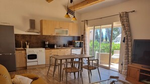 A modern kitchen with wooden cabinets, a dining table, and chairs. There is a sofa and a glass-top coffee table in the living area. - Large Gîte 2 people (LEZIGNAN CORBIERES)
