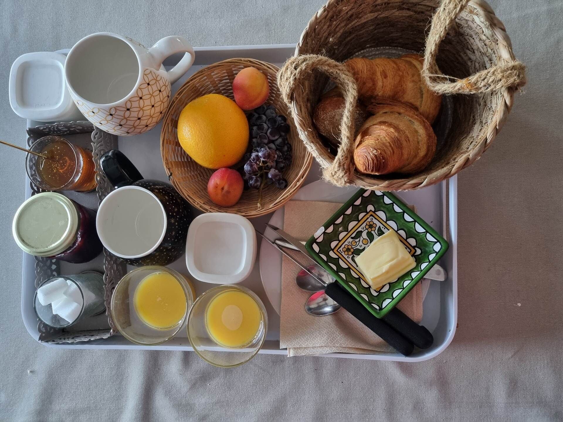 A breakfast tray with croissants, fruits, honey, jam, and butter.