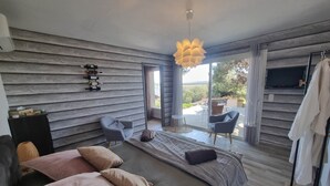 Un dormitorio moderno con cama, dos sillas, televisión y vista al exterior.
