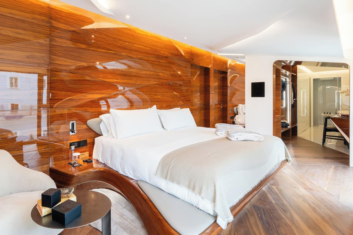 A modern hotel room with a large bed, wooden paneling, a seating area, and a walk-in closet.