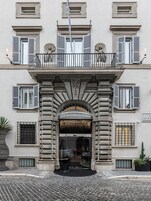 Un edificio con entrada central, varias ventanas con contraventanas y un balcón con barandilla.