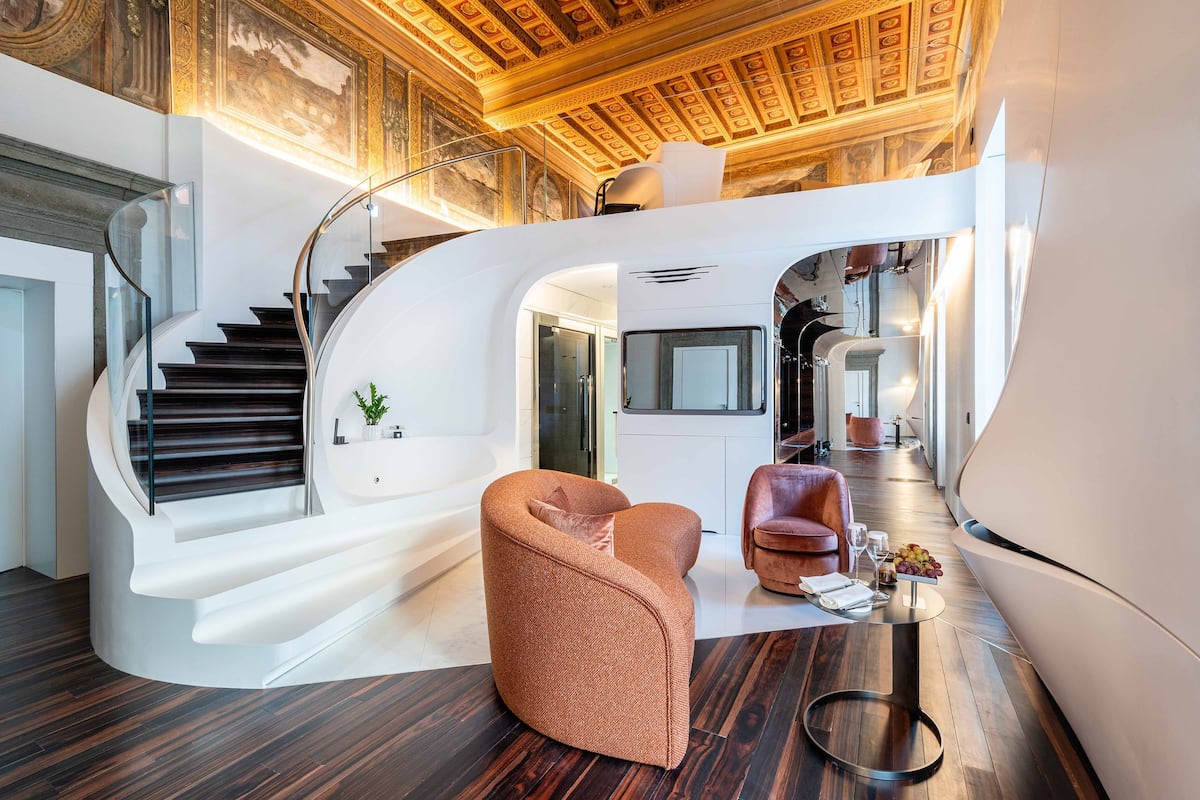 A modern interior with a curved staircase, a seating area, and a view of a kitchen.