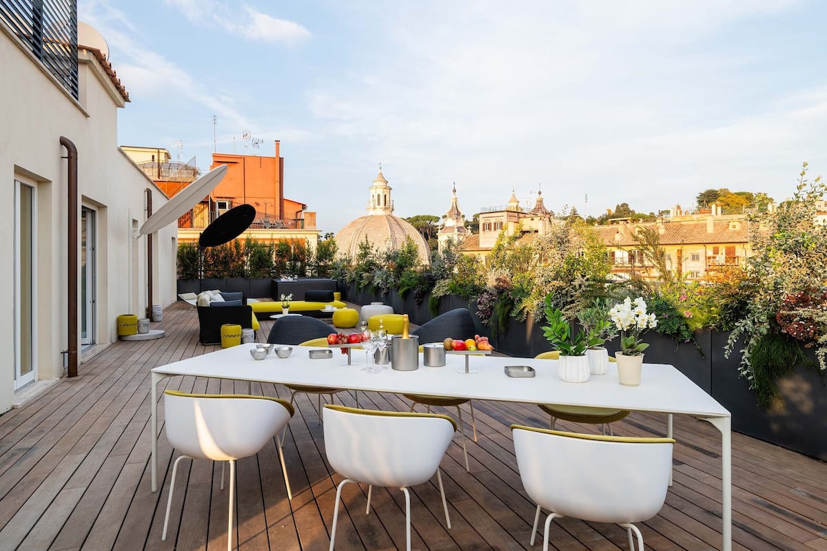 A rooftop patio with a dining table, chairs, and a view of a historic building.