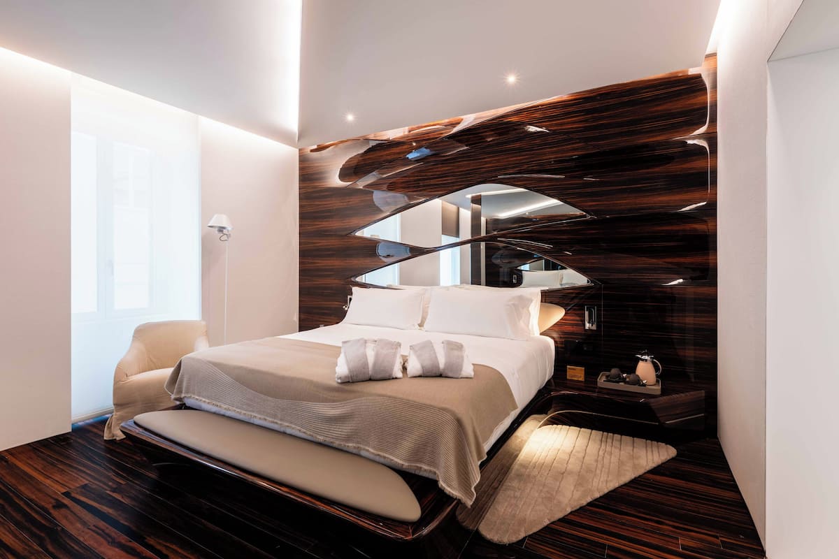 A modern bedroom with a large bed, a bedside table, and a unique wooden wall design.