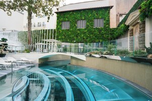 Una piscina con borde de cristal, rodeada de sillas de descanso y barandilla de cristal.