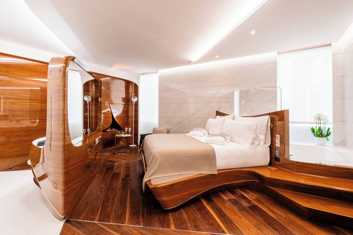 A modern bedroom with a wooden floor, a large bed, a vanity with a mirror, and a window with a plant.