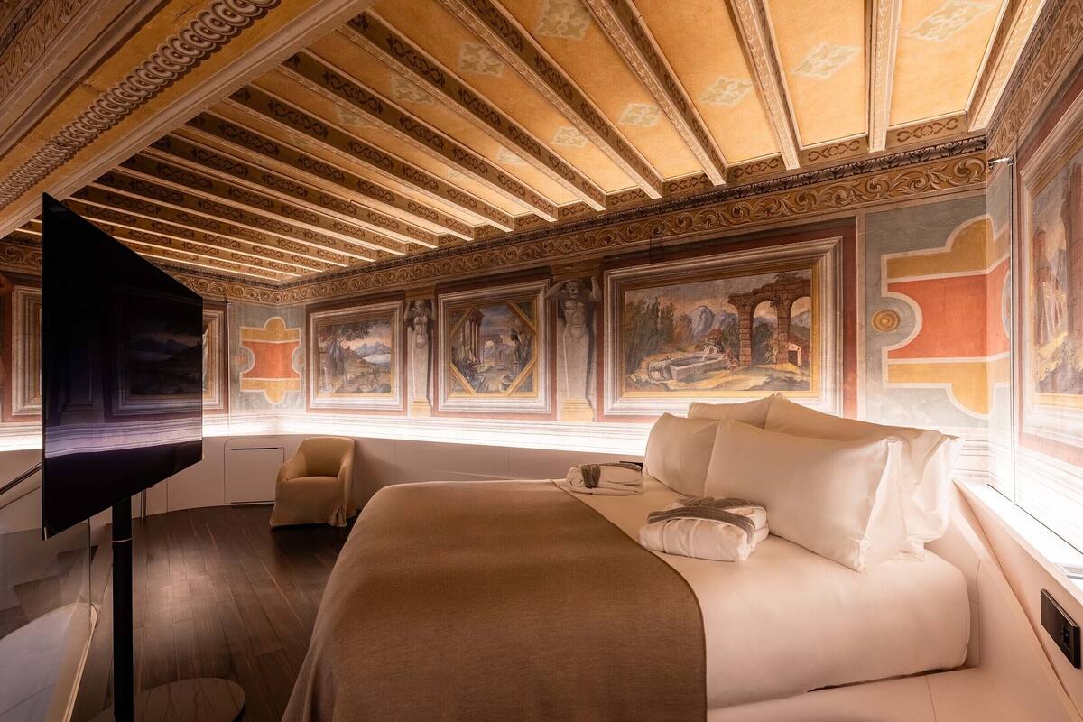 A hotel room with a large bed, a flat-screen TV, a chair, and a mural on the wall.