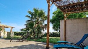 Ein Strandloungebereich mit einem Reetdach, einer Betonwand und einer Palme.