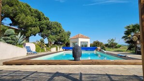 A swimming pool with a wooden deck, a small building with a tiled roof, and surrounding greenery. - Groupe 12 Personnes sur 3 Gîtes (LEZIGNAN CORBIERES)