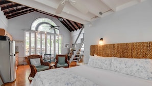 Un dormitorio con una cama grande, un comedor con sillas, una escalera y vistas al exterior.