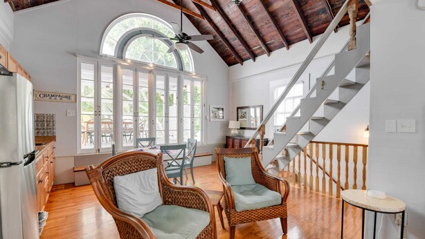 Una habitación amplia con techo de madera, una escalera, sillas de mimbre y un gran ventanal.