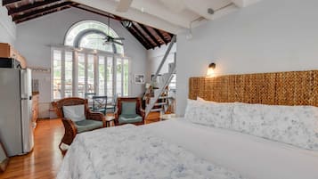 Une chambre avec un grand lit, un coin repas avec des chaises, un escalier et une vue sur l’extérieur.