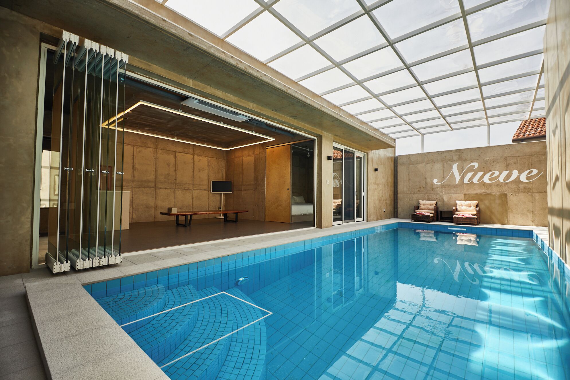 Una piscina interior con techo de vidrio, un banco y dos sillones de descanso.