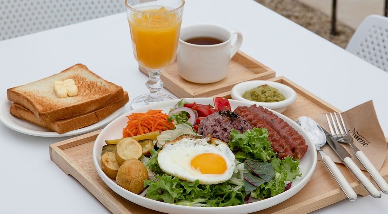Un plateau de petit-déjeuner avec des toasts, un œuf au plat, des légumes et une tasse de café.