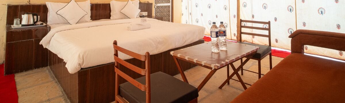 Een hotelkamer met een bed, een houten tafel met stoelen, een nachtkastje en een rood tapijt.