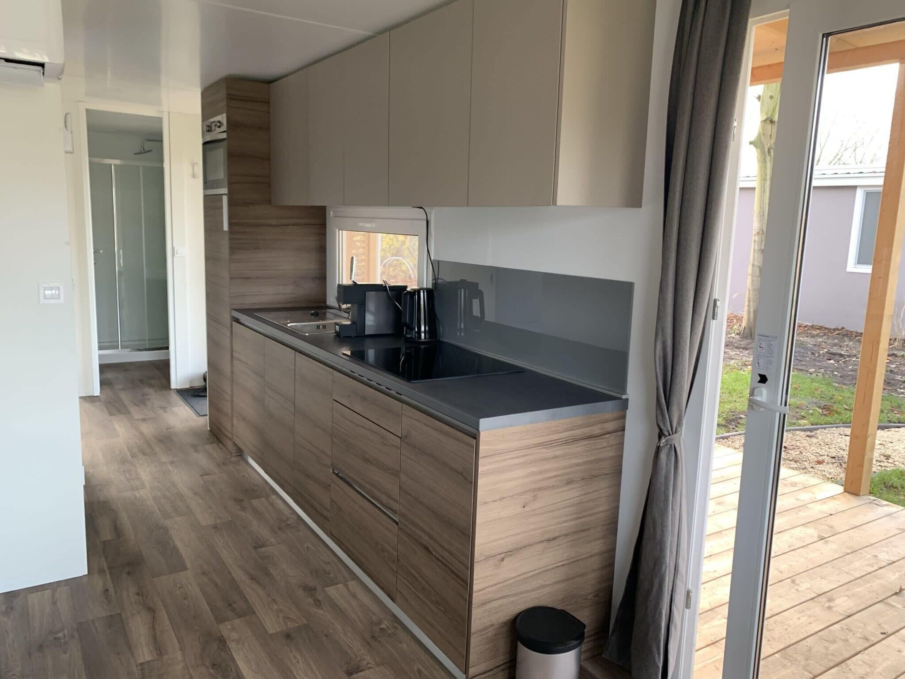 A modern kitchen with wooden cabinetry, a black countertop, and a built-in coffee maker.
