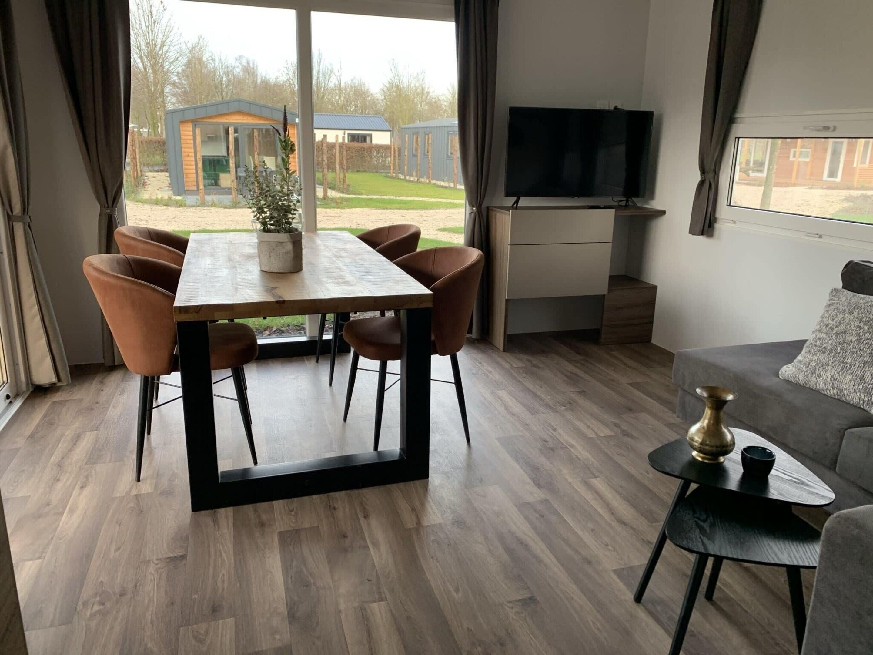 A modern living room with a dining area, a flat-screen TV, and a view of the outside.