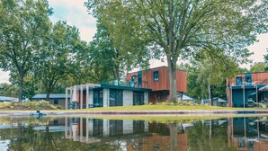 A modern building with a reflection in a calm water body, surrounded by trees. - Charming Chalet 2 km. of the Efteling (Kaatsheuvel)