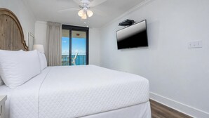 A hotel room with a bed, a ceiling fan, a TV, and a view of the sky.