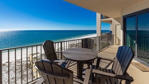 A balcony with a wooden table and chairs, overlooking a beach and the ocean.