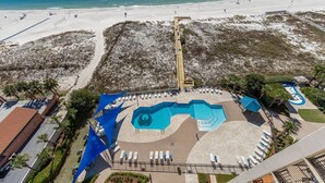 An aerial view of a resort with a large pool, beach access, and a boardwalk leading to the beach.