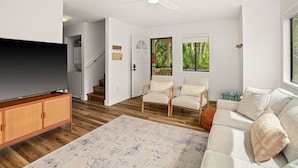 A spacious living room with a flat-screen TV, a wooden floor, a sofa, and a ceiling fan.