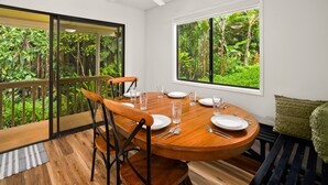 A dining area with a round table set for four, a ceiling fan, and a large window with a tropical view.