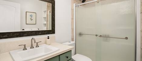 A bathroom with a white sink, green cabinets, a white toilet, and a glass-enclosed shower.