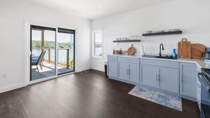A modern kitchen with a large island, a sliding glass door to a deck, and a view of a body of water.