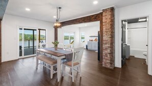 A spacious kitchen with a brick accent wall, a dining area with a large table and white chairs, and a view of a lake through the sliding glass doors.