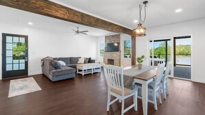 A spacious living room with a fireplace, a dining area with white chairs, a gray sofa, and a ceiling fan.