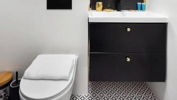 Un baño moderno con inodoro blanco, tocador negro con espejo y baldosas de suelo con diseño.