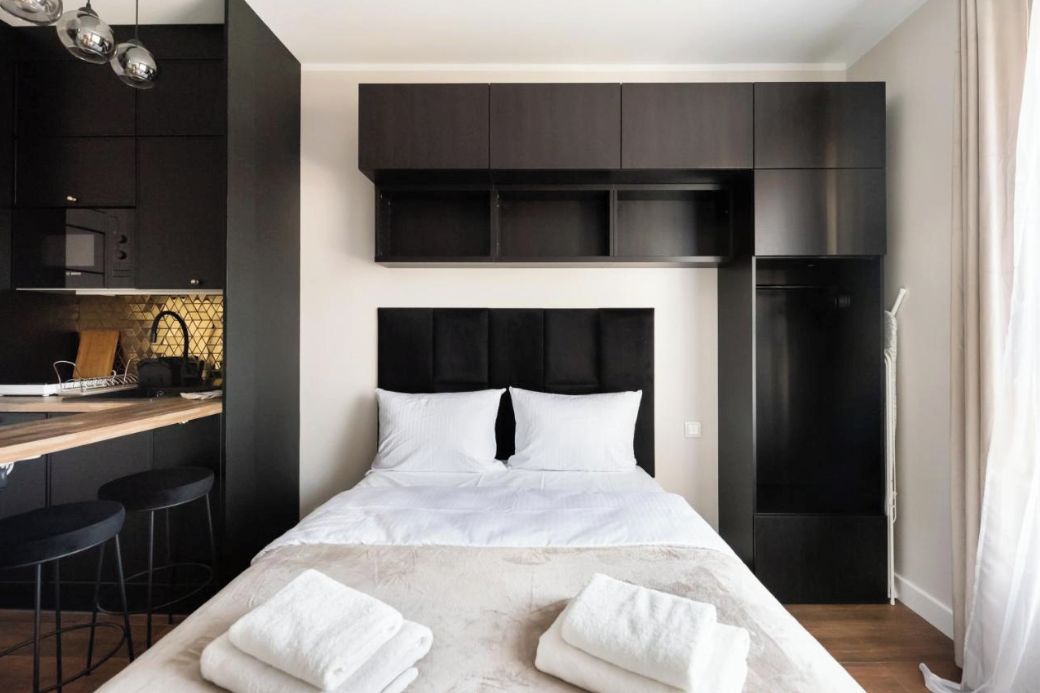 A modern hotel room with a large bed, a kitchen area, and a dining space.