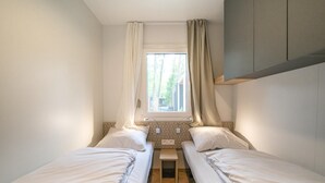 Una habitación pequeña y luminosa con dos camas individuales, una ventana con cortinas y una mesita.