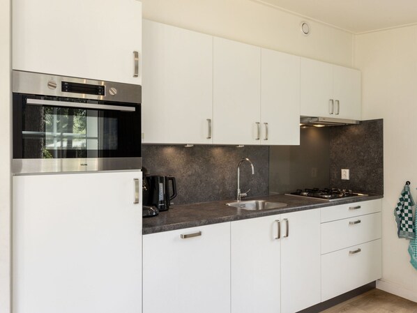 A modern kitchen with white cabinets, a stainless steel oven, a coffee maker, and a sink. - Chalet in De Peel Near Forest (Vlierden)