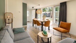 A modern living room with a sofa, a dining table with chairs, a coffee table with glasses, and a hanging light fixture. - Chalet in De Peel Near Forest (Vlierden)