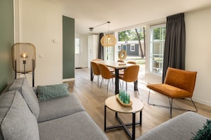 Un salon moderne comprenant un canapé, une table à manger avec des chaises, une table basse avec des verres et un luminaire suspendu.