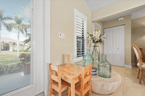 A dining area with a wooden table and chairs, a vase with flowers, and a glass bottle. - S Exposure Waterfront Home | Near Beach/Food/Fun (Marco Island)
