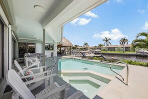 A pool area with lounge chairs, a hot tub, and a view of a resort with palm trees and a building in the background. - S Exposure Waterfront Home | Near Beach/Food/Fun (Marco Island)