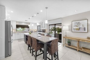 A modern kitchen with a central island, white cabinetry, and pendant lighting. - S Exposure Waterfront Home | Near Beach/Food/Fun (Marco Island)