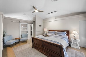 Une chambre à coucher avec un lit en bois, un ventilateur de plafond, une table de chevet blanche et une chaise.
