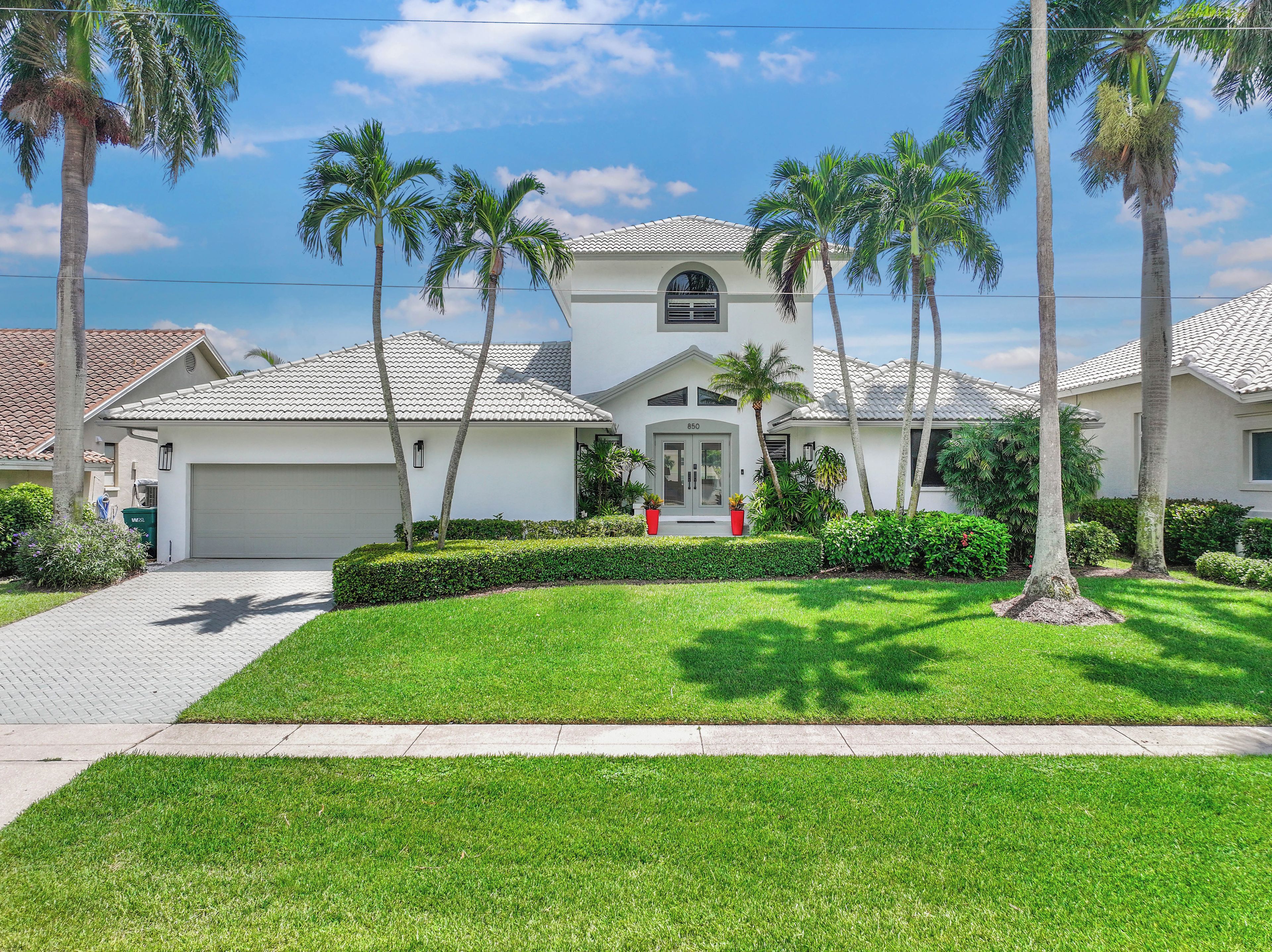A residential house with a white exterior, a garage, and a well-maintained lawn with palm trees.