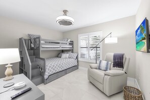 A bedroom with a bunk bed, a sofa, a lamp, a remote control, and a ceiling fan.